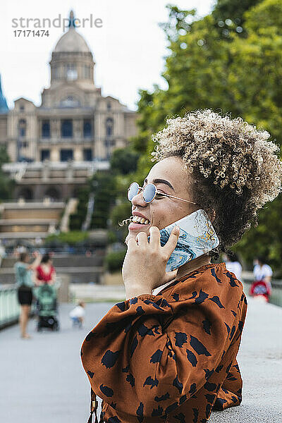 Modische Frau  die lacht  während sie mit einem Smartphone in der Stadt spricht