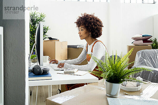 Afro-Frau  die einen Computer benutzt  während sie in ihrer neuen Wohnung von Kartons umgeben ist