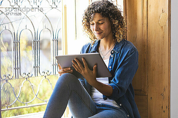 Smiling woman using digital tablet while sitting by window at home