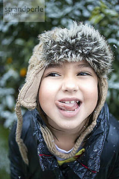 Mischievous girl in warm clothing sticking out tongue during snow
