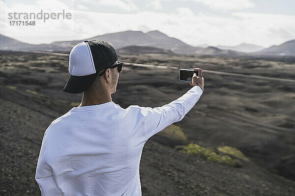 Männlicher Tourist mit Hut macht ein Selfie auf dem Vulkan El Cuervo  Lanzarote  Spanien  während des Urlaubs