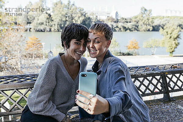 Lächelnde Freunde  die ein Selfie mit dem Handy machen  während sie im Freien sitzen