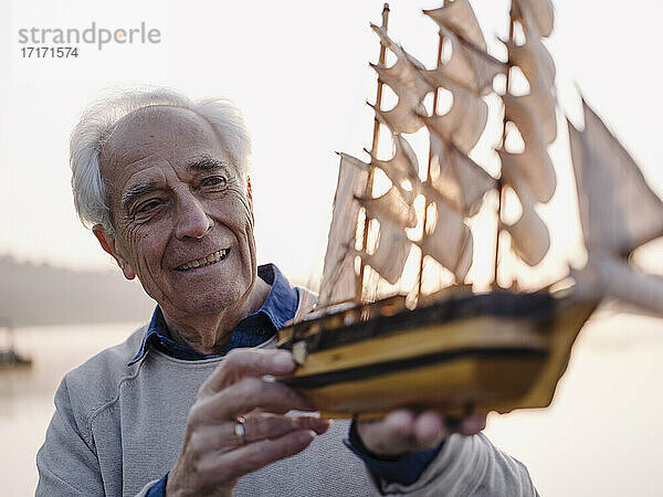Lächelnder Mann  der im Freien stehend ein Segelschiff-Spielzeug untersucht