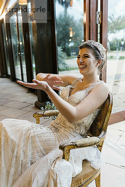Happy bride clapping hands while sitting on chair at banquet