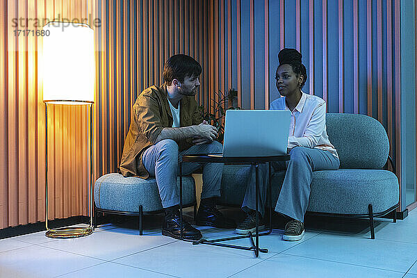 Männliche und weibliche Kollegen mit Laptop  die an einem beleuchteten Arbeitsplatz sitzen und planen