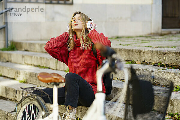 Blond woman listening music through headphones while sitting on steps