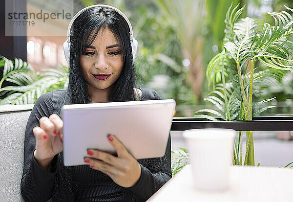 Beautiful young woman listening music while using digital tablet at cafe