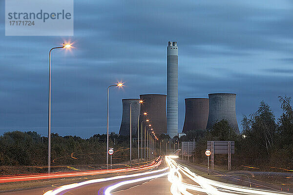 UK  England  Rugeley  Fahrzeug-Lichtspuren entlang der beleuchteten Straße in der Abenddämmerung mit Kühltürmen im Hintergrund