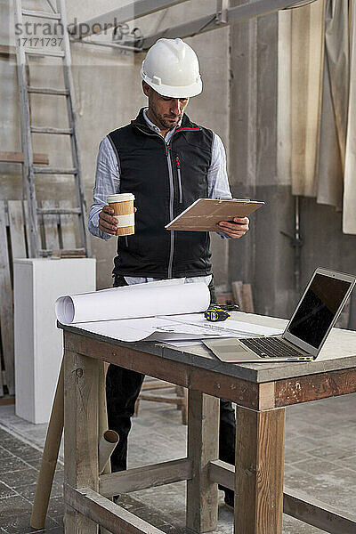 Männlicher Architekt mit Kaffee in der Hand bei der Analyse eines Plans in einem Gebäude