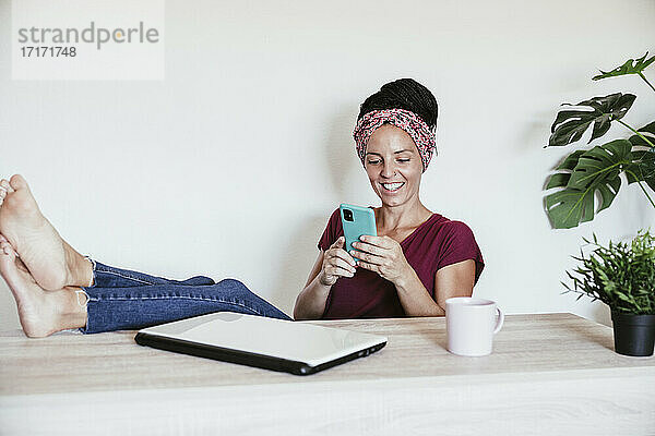 Eine Unternehmerin ruht sich aus  während sie ihr Smartphone im Büro zu Hause an der Wand benutzt