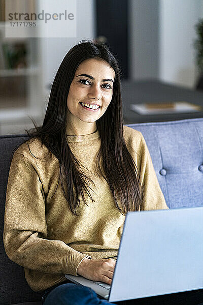 Woman with laptop smiling while sitting at home