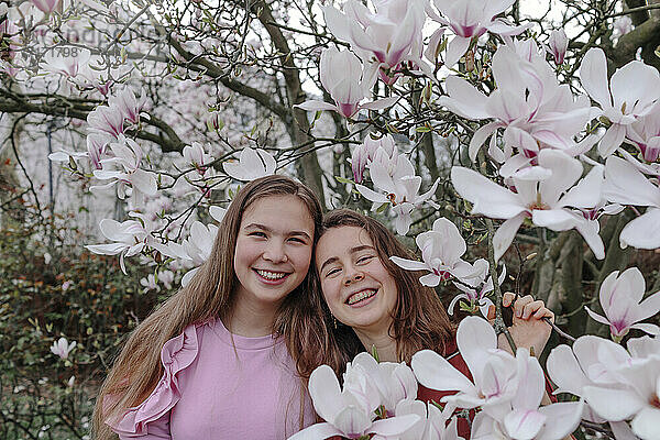 Happy female friends by magnolia trees in park