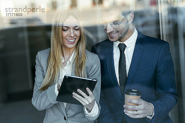 Lächelnde Geschäftsfrau  die mit einem Kollegen über einem digitalen Tablet arbeitet  während sie im Büro steht