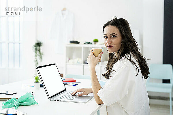 Ärztin beim Kaffee trinken und Online-Beratung am Schreibtisch in der Klinik