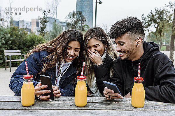 Cheerful female friends with young man using smart phone