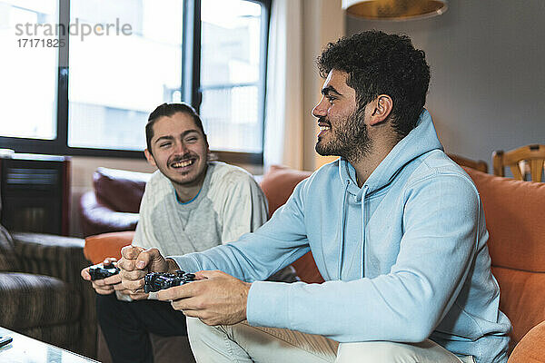 Lächelnde junge Freunde  die sich beim Spielen eines Videospiels zu Hause unterhalten
