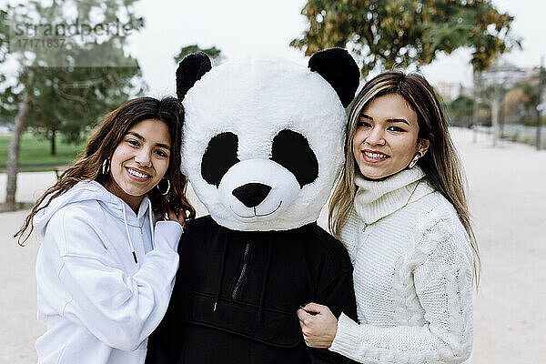 Smiling female friends with male friend wearing panda mask