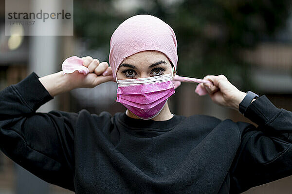 Female cancer patient in bandana wearing pink protective face mask during COVID-19