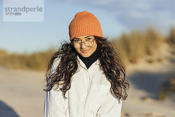 Smiling beautiful woman in orange knit hat against sky during sunny day
