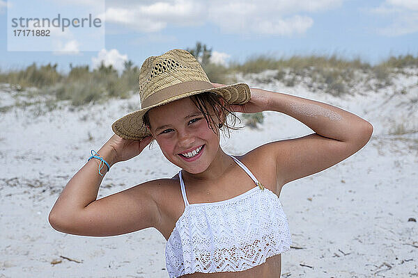 Lächelndes Mädchen mit Hut  das am Strand steht