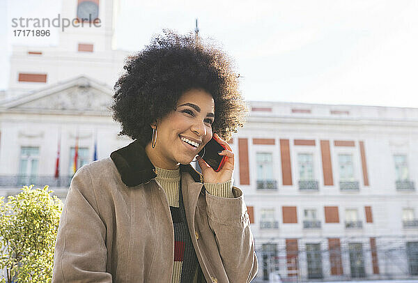 Smiling woman talking on mobile phone while standing in city