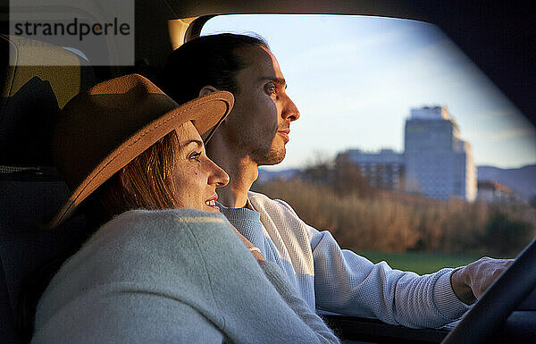 Man driving car while female embracing during sunset