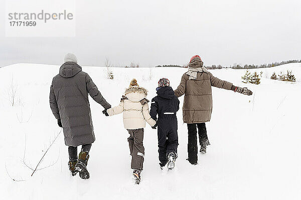 Eltern mit Kindern spazieren auf schneebedeckter Landschaft gegen den Himmel