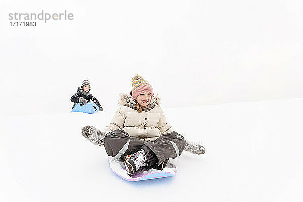 Verspielte Geschwister beim Schlittenfahren auf einem verschneiten Hügel