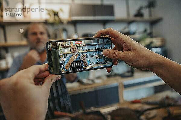 Woman filming chef through mobile phone while standing in kitchen