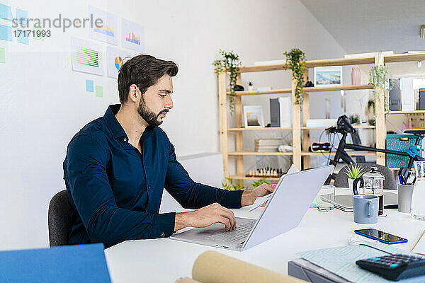 Male entrepreneur looking at document while using laptop in office