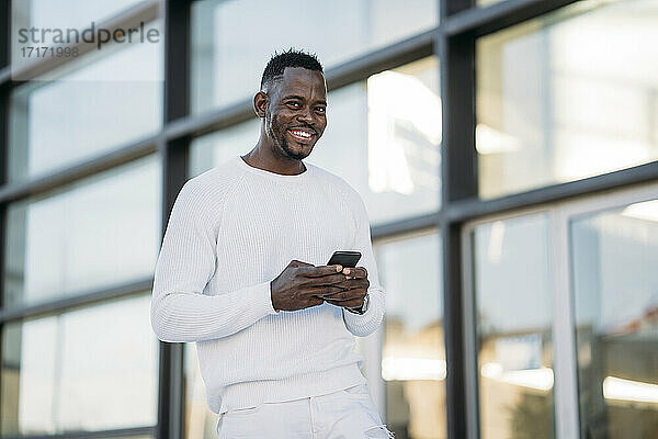 Fröhlicher Mann mit Smartphone  der an einem Gebäude steht