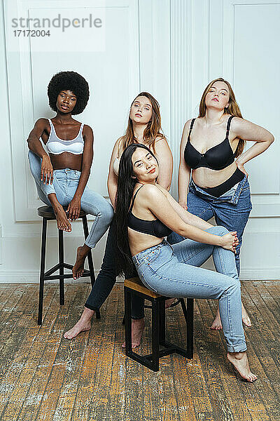 Selbstbewusste multiethnische Gruppe von Frauen in BHs und Jeans  die gegen eine Wand posieren