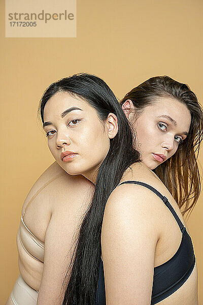 Multi-ethnische weibliche Modelle in Dessous lehnen sich gegenseitig auf die Schulter vor gelbem Hintergrund