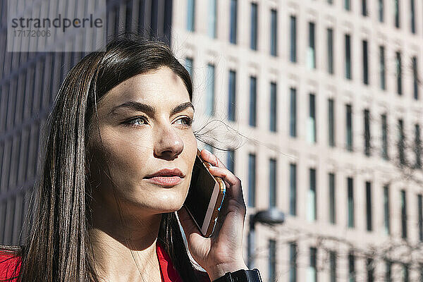 Beautiful businesswoman talking on mobile phone while looking away against building