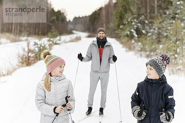 Vater mit Kindern beim Skifahren in einer verschneiten Landschaft im Wald