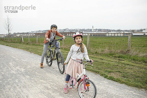 Bruder und Schwester mit Fahrrädern auf der Straße gegen den klaren Himmel