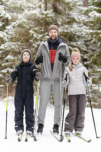 Vater und Kinder beim Skifahren gegen Bäume im verschneiten Wald