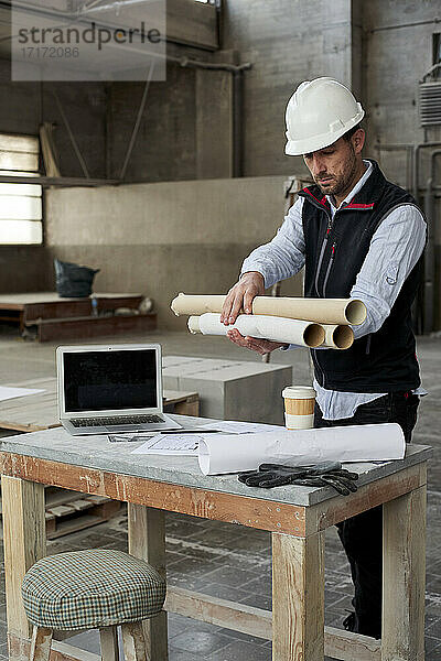 Männlicher Ingenieur hält Blaupausen  während er an einem Tisch in einem Gebäude steht