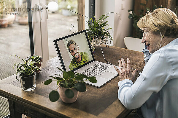 Glückliche ältere Frau bei einem Videoanruf mit ihrem Enkel  während sie zu Hause am Tisch sitzt