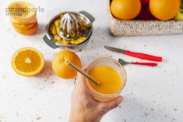 Frau hält Orangensaftglas mit Trinkhalm über modernem Terrazzomarmor