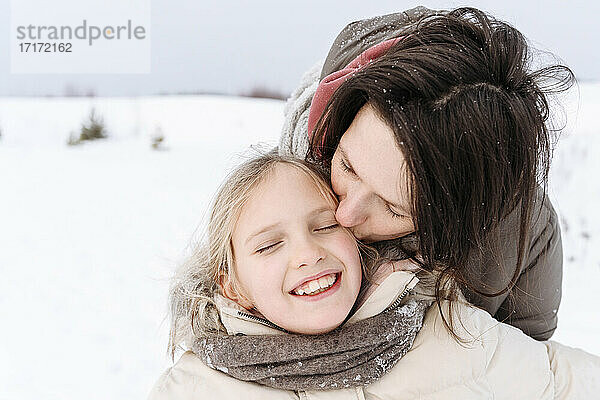 Nahaufnahme einer Mutter  die ihre lächelnde Tochter im Winter küsst