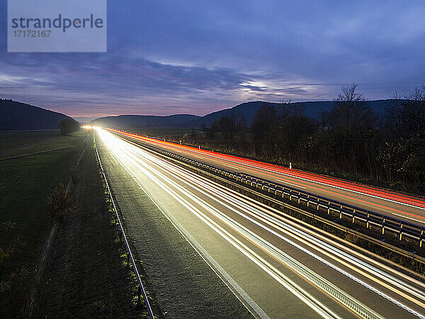 Light trails on motorway against cloudy sky