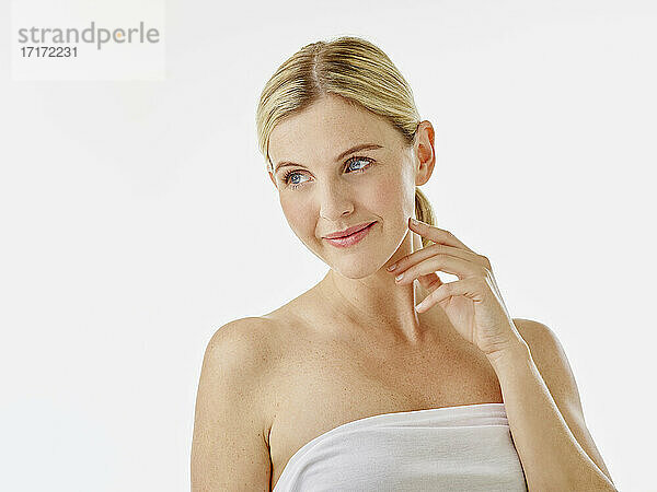 Young woman wearing towel looking away while standing against white background