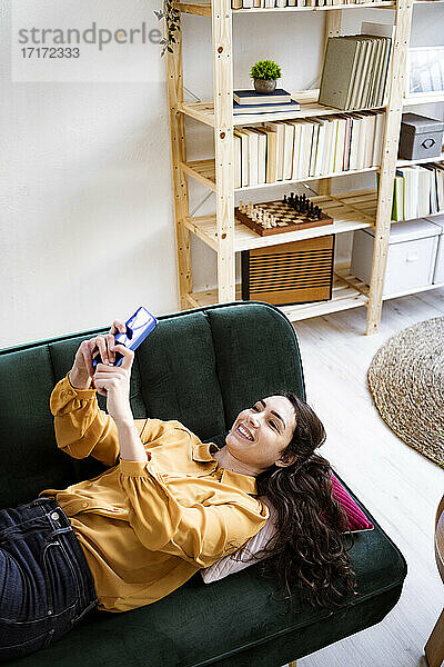 Woman using mobile phone while lying on sofa at home