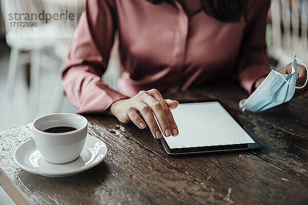 Die Hand einer Geschäftsfrau benutzt ein digitales Tablet am Tisch in einem Café während der COVID-19