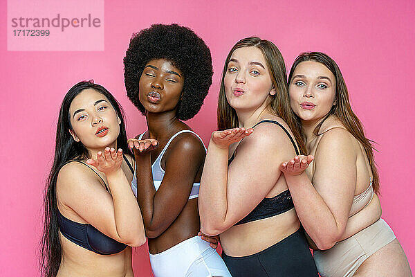 Multi-ethnische Gruppe von weiblichen Modellen in Dessous bläst Küsse vor rosa Hintergrund