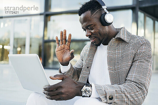 Mann trägt Kopfhörer und gestikuliert bei einem Videotelefonat mit einem Laptop