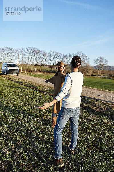 Heterosexual couple with arms outstretched standing on green land during sunset