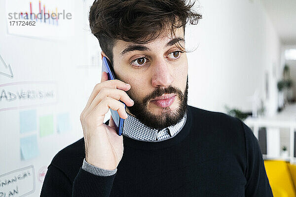 Geschäftsmann im Gespräch am Telefon vor einer Tafel im Büro