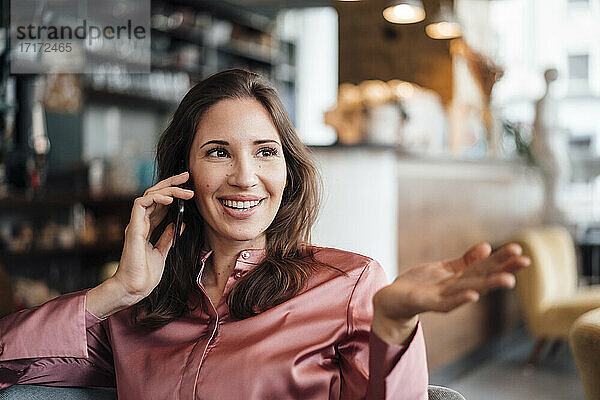 Lächelnde weibliche Freiberuflerin gestikuliert  während sie mit ihrem Smartphone in einem Café spricht
